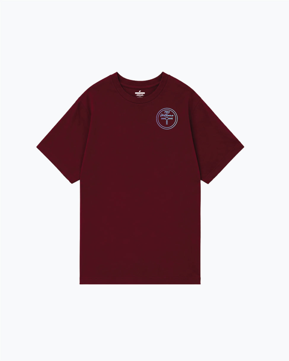 Maroon crewneck tee with small circular badge graphic on chest